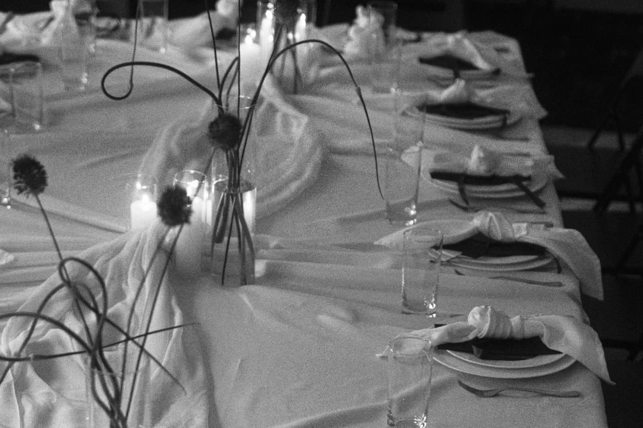 Black-and-white photograph of a candlelit Cureators table set with linen and knotted napkins